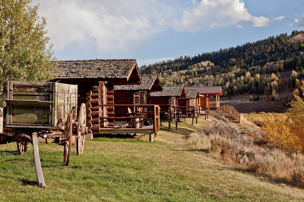 Goosewing Ranch met houten huisjes op een rij in het groen met uitzicht op bergen en bomen/bossen in Wyoming