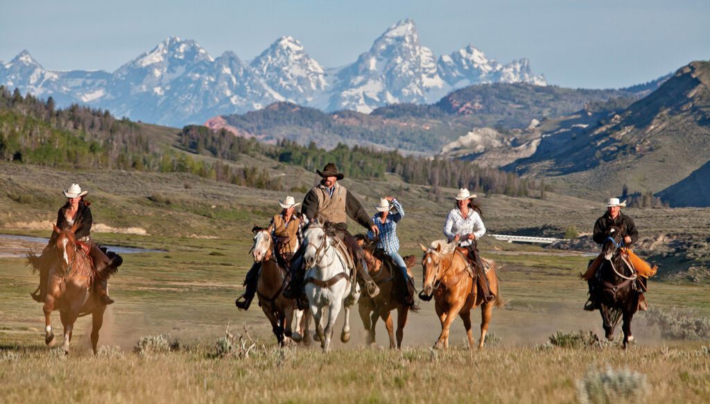 mensen die paardrijden met cowboyhoeden op, cowboys en cowgirls die paardrijden in de velden tussen de bergen